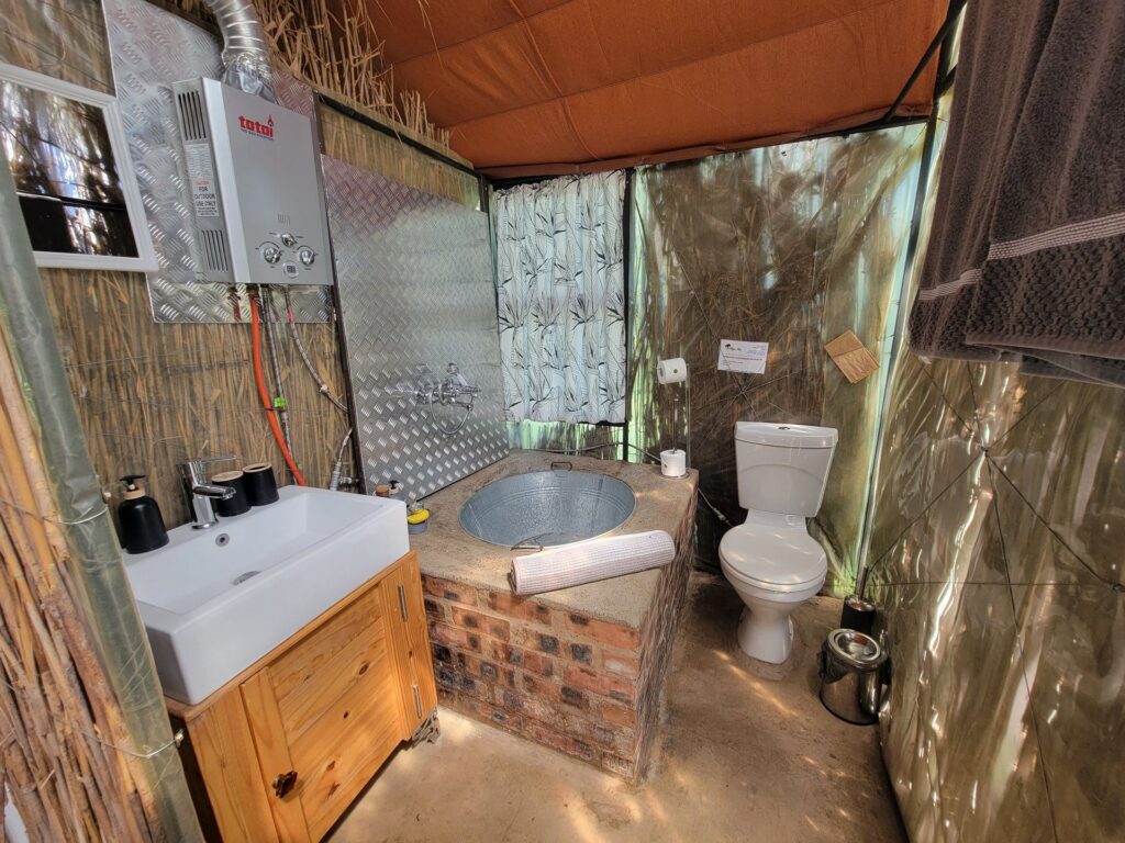 Bathroom at the River Stay with a galvanised tin bath set into brickwork, basin and gas geyser