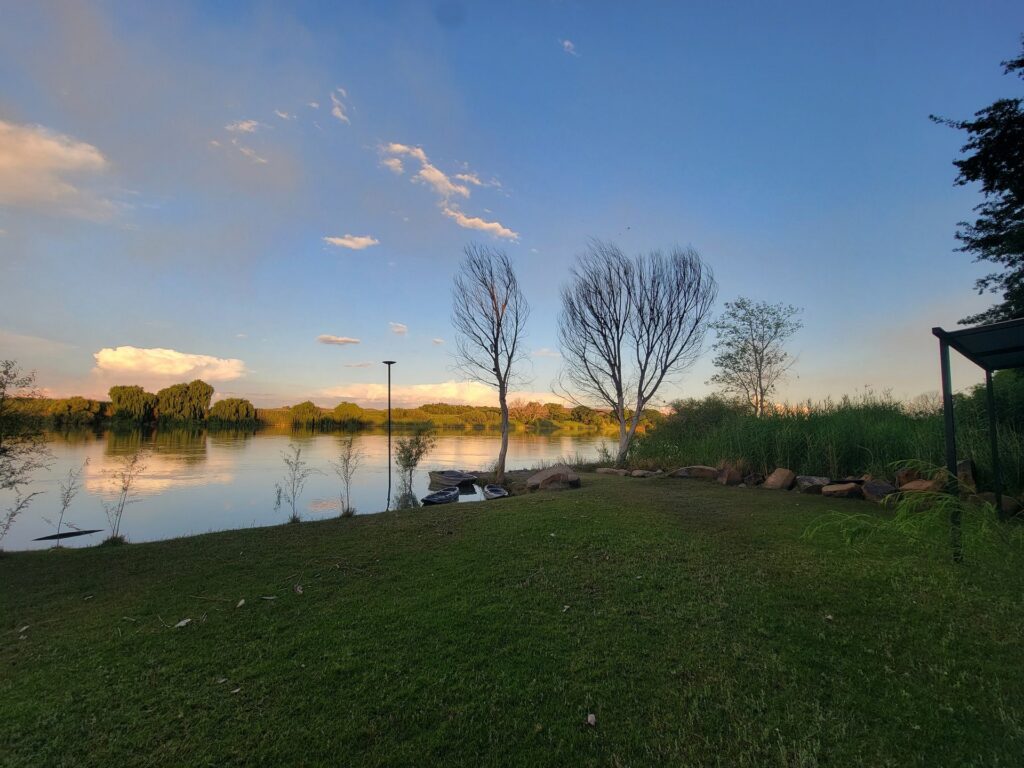 Lawn running down to the Orange River at sunset with a kayak pulled up on the bank