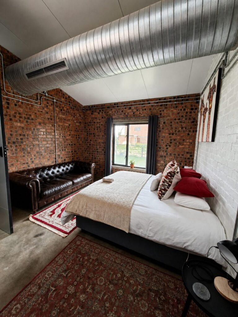 Hoofslaapkamer by die Vakansie Huis met ’n kingbed, leer-chesterfield en sigbare baksteenmure