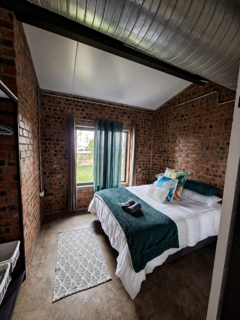 Tweede slaapkamer by die Vakansie Huis met ’n queenbed, blougroen gooikombers en ’n venster op die tuin